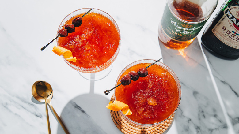 Overhead view of two frozen Manhattan cocktails with two liquor bottles and two spoons.