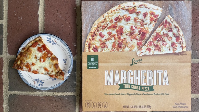 Slice of Margherita pizza topped with chunks of tomato on plate, alongside box on brick surface
