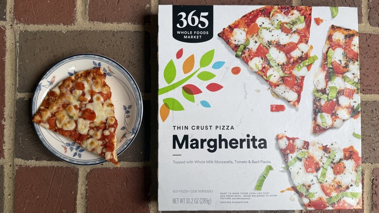 Slice of 365 Margherita pizza topped with tomatoes and mozzarella, alongside box on brick surface