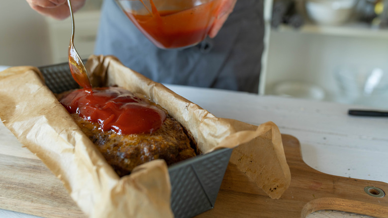Home cook glazing a homemade meatloaf in a paper-lined pan
