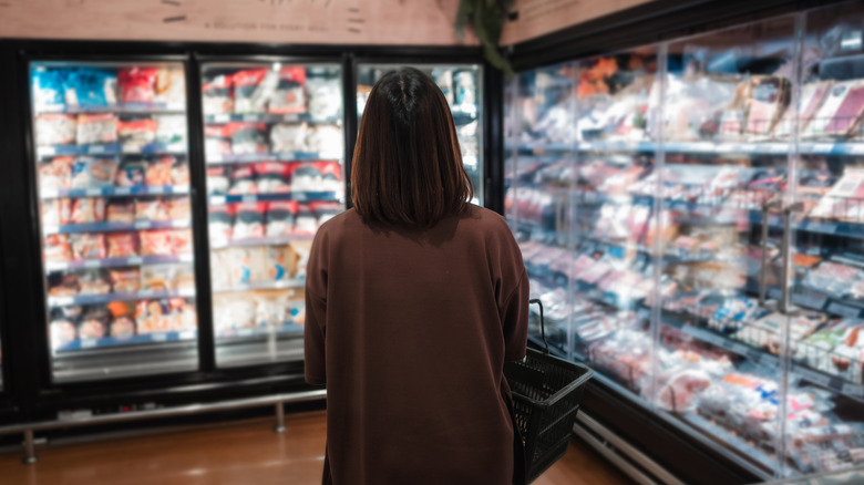 Person standing in front of a freezer aisle with basket in arms