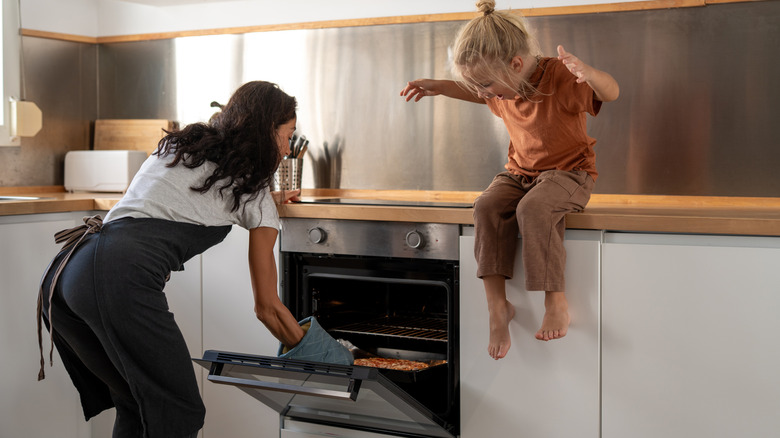 Mom getting pizza out of oven with little girl on countertop
