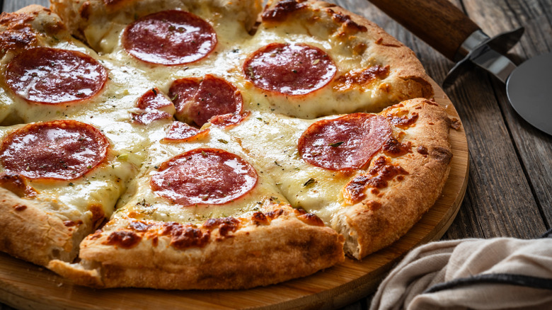 A sliced pepperoni pizza on a wooden table next to a pizza cutter and a cloth