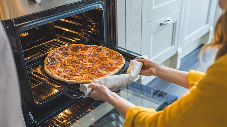 a person in a yellow shirt removing a pizza from the oven on a baking sheet
