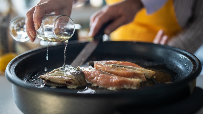 Hands adding alcohol to cooking fish in pan