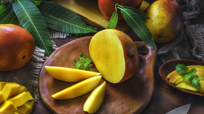 mango fruits displayed on a table and platters, some cut, some whole