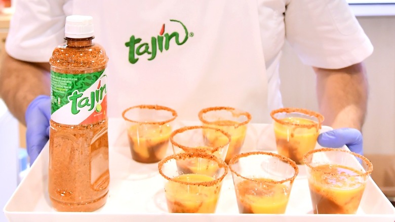 person with tray of Mexican fruit cups with tajin seasoning and bottle of tajin alongside