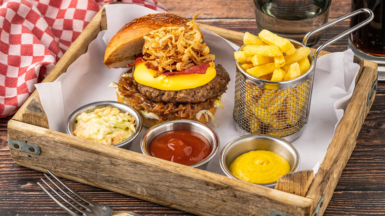 A cheeseburger topped with tobacco onions alongside fries and dipping sauces