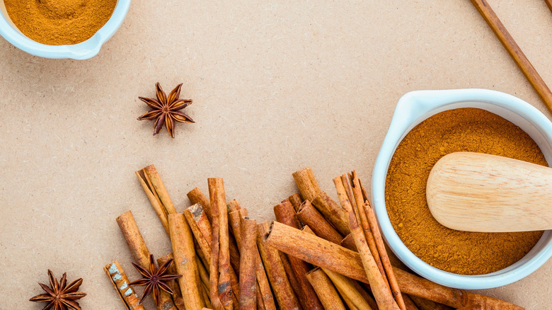 Overhead shot of whole cinnamon sticks and star anise beside two bowls filled with spice powder