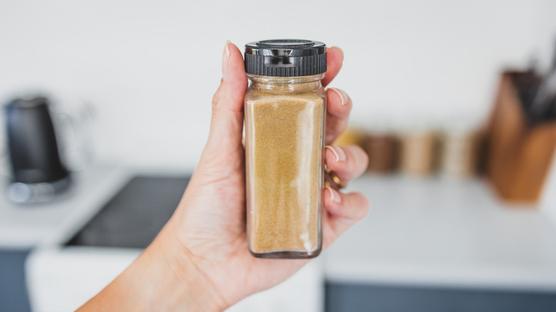 Hand holding glass container of garam masala in kitchen