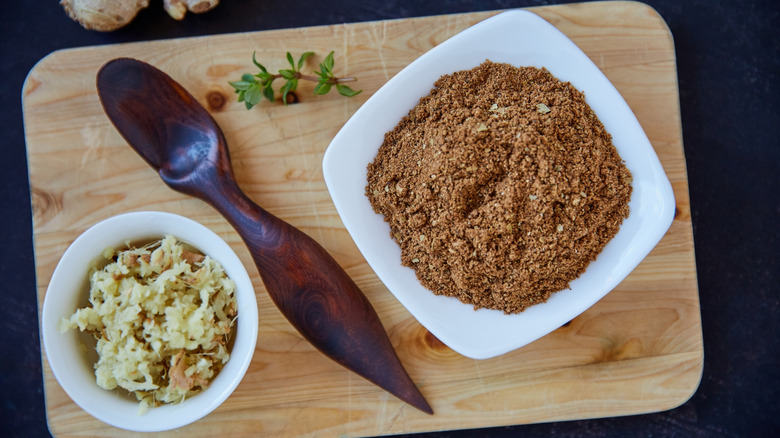 Garam masala in bowl alongside other cooking ingredients and spoon on wooden cutting board