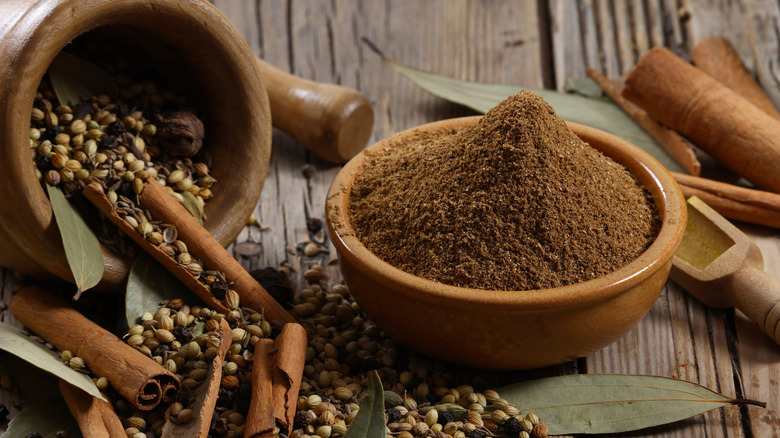 Garam masala in bowl alongside raw spices like coriander seeds, cinnamon, and bay leaves