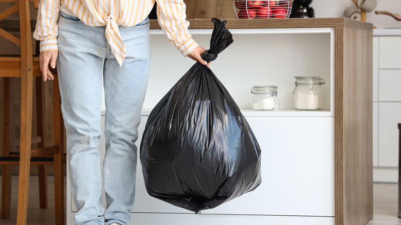 Person holding black plastic garbage bag inside kitchen