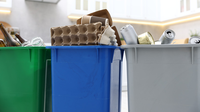 Three plastic garbage bins with metal cans, cardboard and paper waste, and glass bottles inside