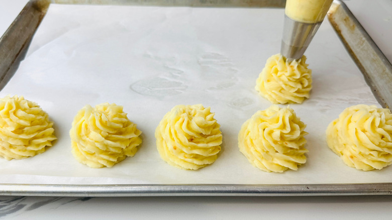 Piping duchess potato rosettes onto baking sheet
