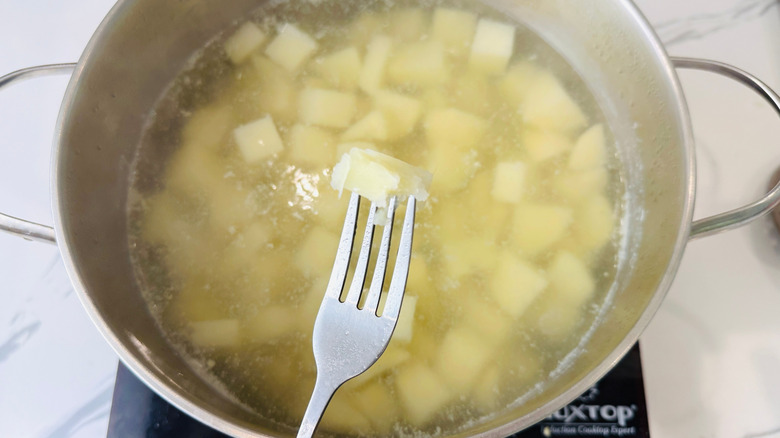 Fork holding tender potato cube over pot of boiling potatoes