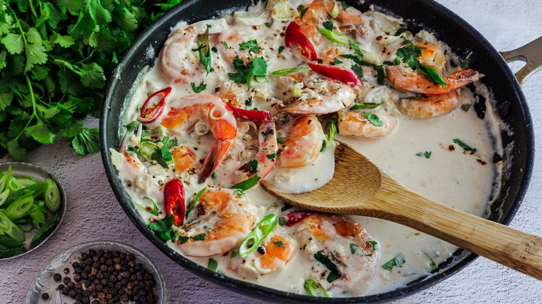Shrimp in coconut milk in a pan with scallions and cilantro on the side