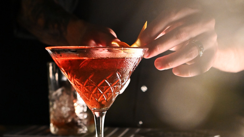 Bartender garnishing red cocktail in martini glass with citrus peel