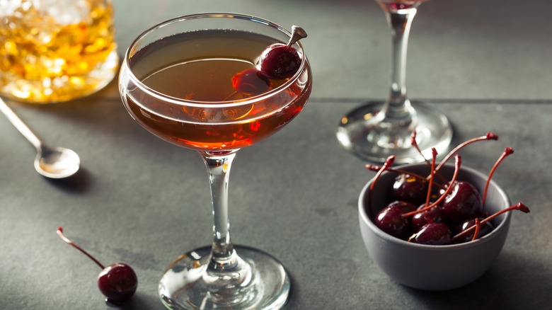 Manhattan cocktail, garnished with skewered cherries next to cherry bowl
