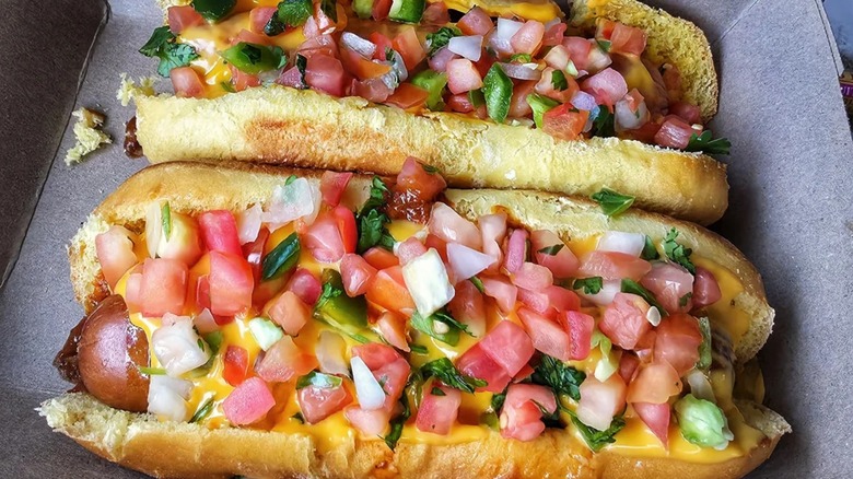 Two hot dogs with tomatoes, cheese, and peppers