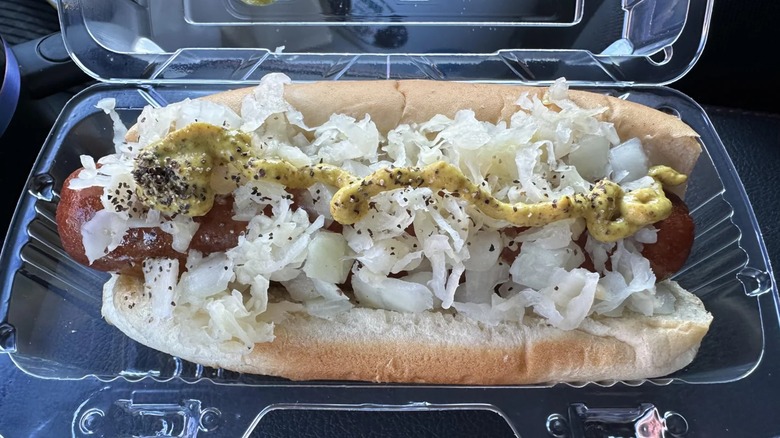 Hot dog in plastic clamshell with mustard, onions, and sauerkraut
