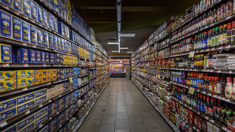 A symmetrical view of an empty grocery store aisle, with shelves lined with products on either side