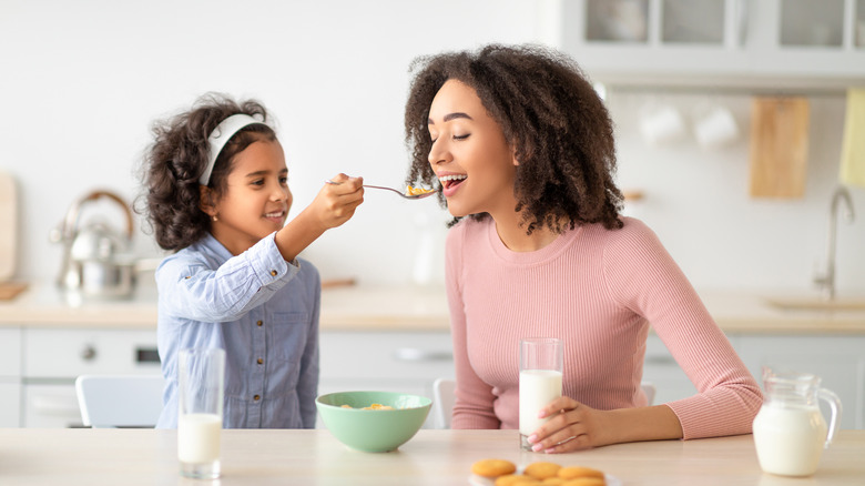 Child spoon feeding cereal to mother 