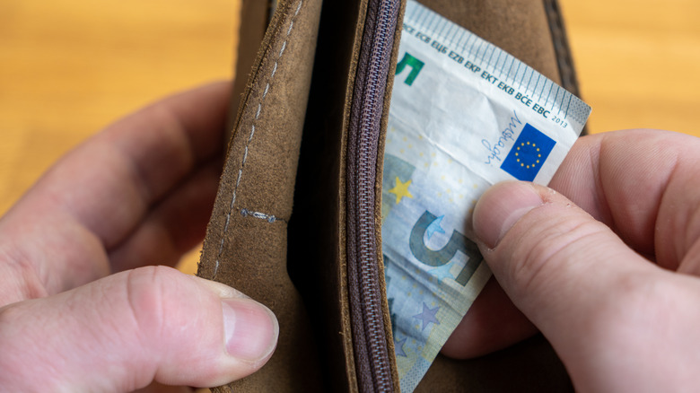 Hands pulling a 5-euro note out of a wallet