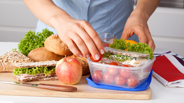 Woman packing sandwiches, cherry tomatoes, and fruits into a container