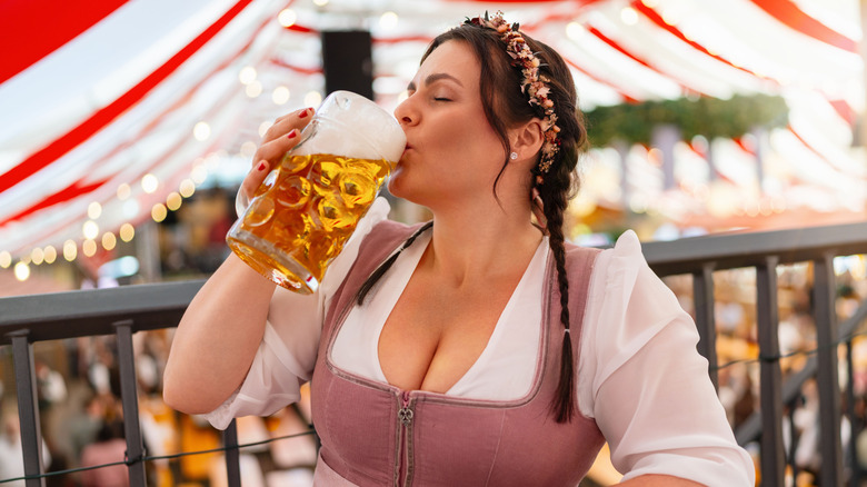 Woman in a dirndl drinking beer under a tent