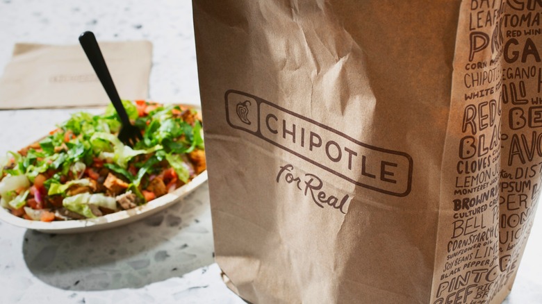 Brown paper bag with Chipotle logo with burrito bowl in background
