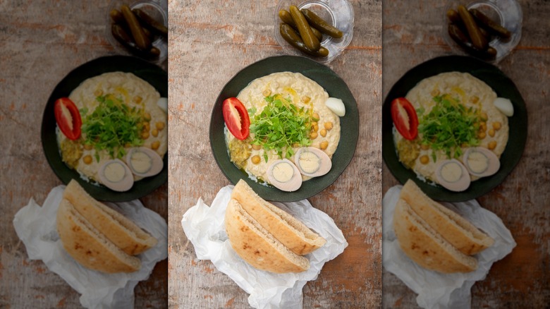 bowl of hummus and plate of pickles on wood surface