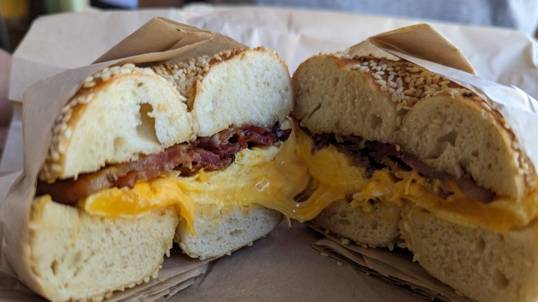 A bodega-style bacon, egg, and cheese sandwich wrapped in paper and cut in two to reveal its cross-section