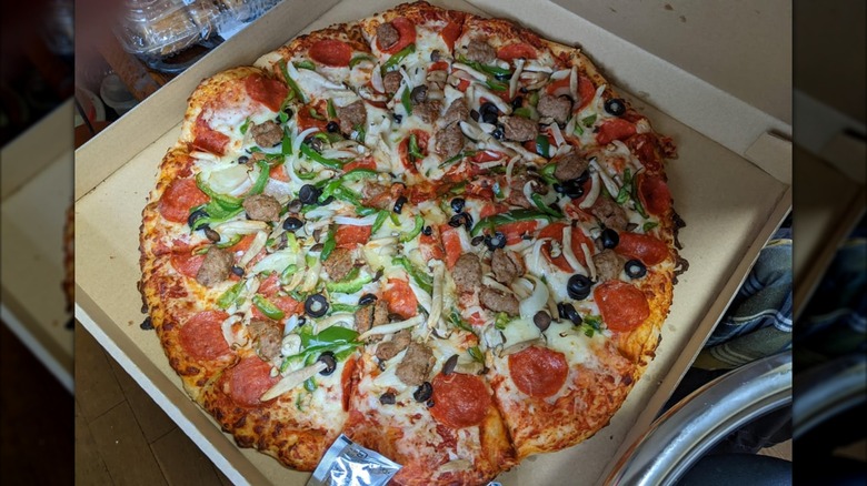 A Costco Combo pizza sitting in a cardboard takeout box on a kitchen counter