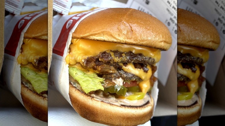 In-N-Out triple cheeseburger with pickles and chopped chilis in paper sleeve