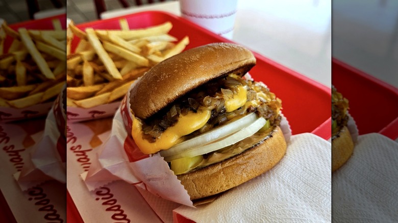 In-N-Out burger with cheese and both raw and grilled onions on red tray next to box of fries