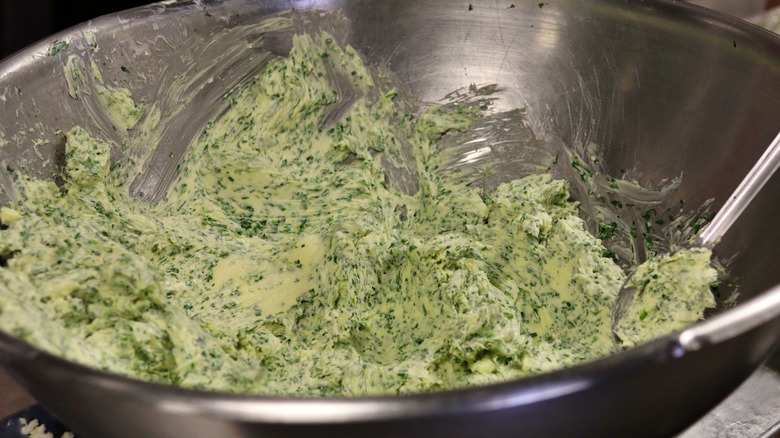 Herbs and butter being mixed in a metal bowl