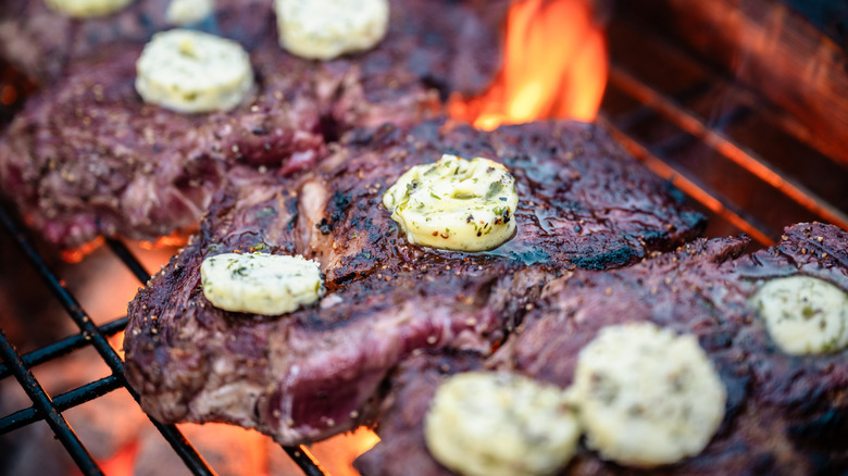 Ribeye steaks being grilled over flame, topped with compound herb butter