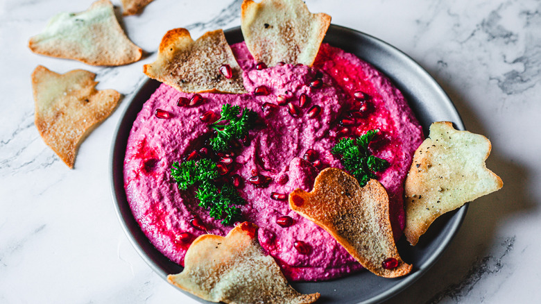 Magenta hummus on a plate with parsley, pomegranate and ghost chips