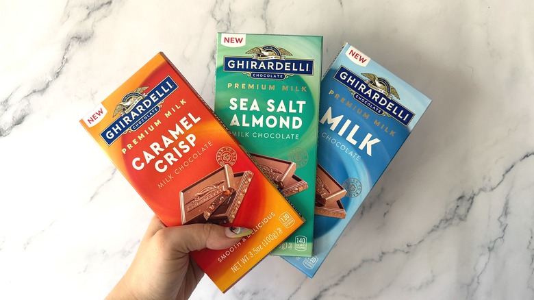 Hand holding three Ghirardelli Milk Chocolate bars against marble background