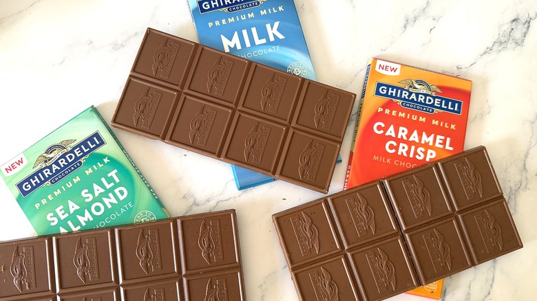 Three unwrapped Ghirardelli milk chocolate bars on cases on marble surface