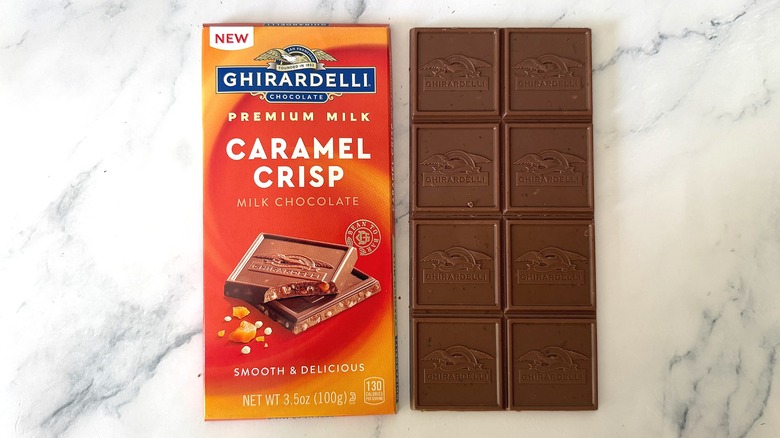 Unwrapped bar of Ghirardelli Caramel Crisp Milk Chocolate next to wrapper on marble surface