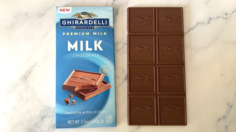 Unwrapped bar of Ghirardelli Milk Chocolate next to wrapper on marble surface
