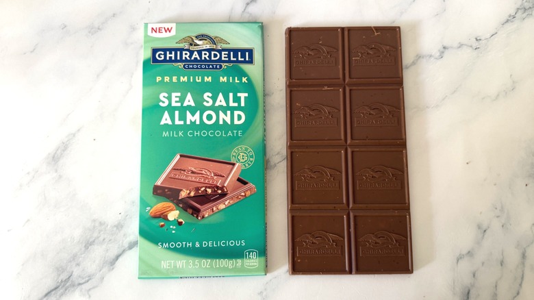 Unwrapped bar of Ghirardelli Sea Salt Almond Milk Chocolate next to wrapper on marble surface