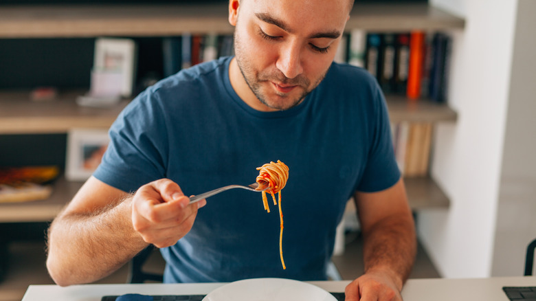 Young man eating spaghetti with a fork