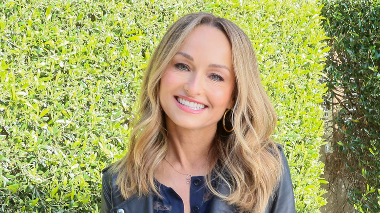 Headshot of Giada de Laurentiis smiling standing in front of a hedge