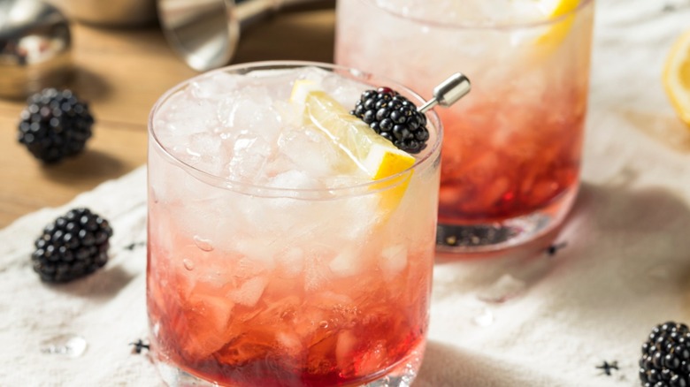a gin bramble cocktail with fresh blackberries and a lemon wedge against a light beige and tan background.