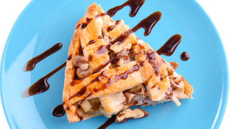 A slice of apple pie drizzled with chocolate sauce sits on a blue plate.
