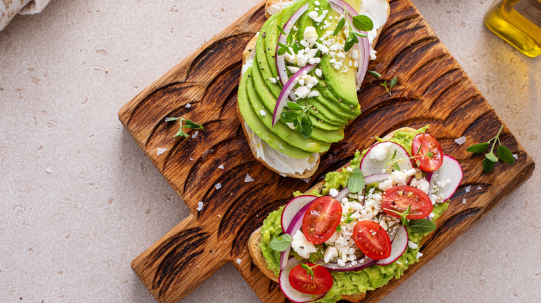 Two avocado toasts with tomatoes, feta cheese, and red oinions