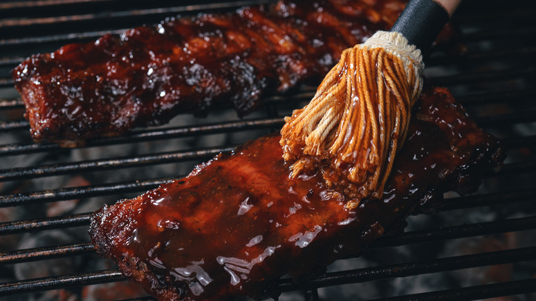 Brushing BBQ sauce on meat on a grill